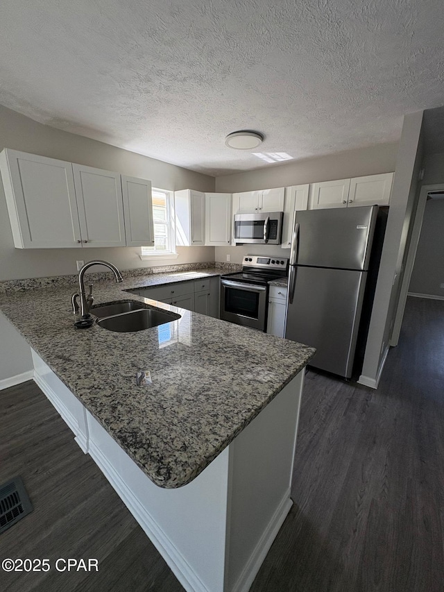 kitchen with a sink, stainless steel appliances, light stone counters, a peninsula, and dark wood finished floors
