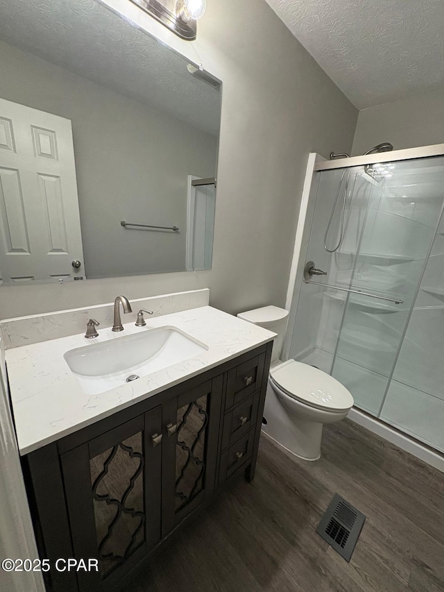 bathroom featuring a textured ceiling, visible vents, a stall shower, toilet, and wood finished floors