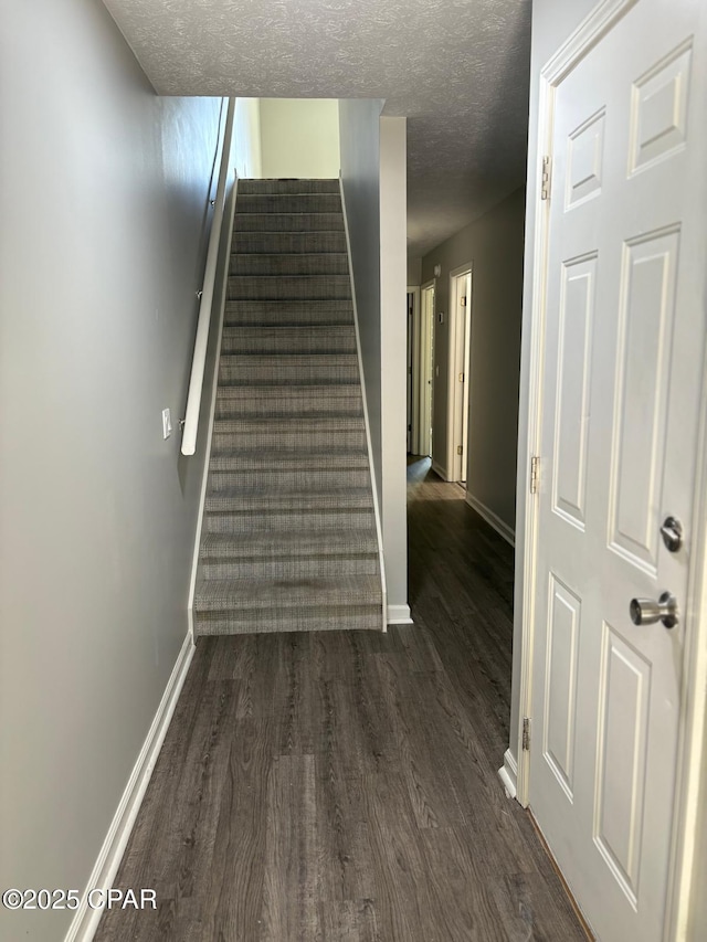 staircase with baseboards, wood finished floors, and a textured ceiling