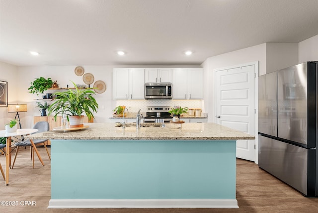 kitchen with light stone countertops, a sink, white cabinets, light wood-style floors, and appliances with stainless steel finishes