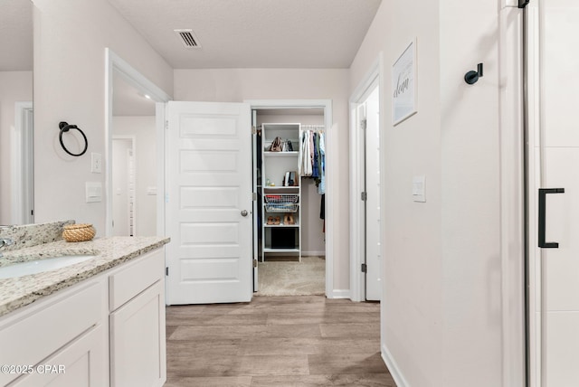 bathroom with visible vents, a walk in closet, baseboards, wood finished floors, and vanity