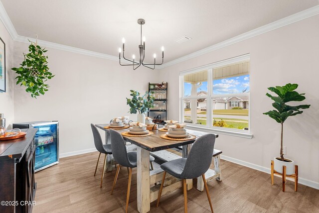 dining space featuring an inviting chandelier, baseboards, crown molding, and light wood-style floors