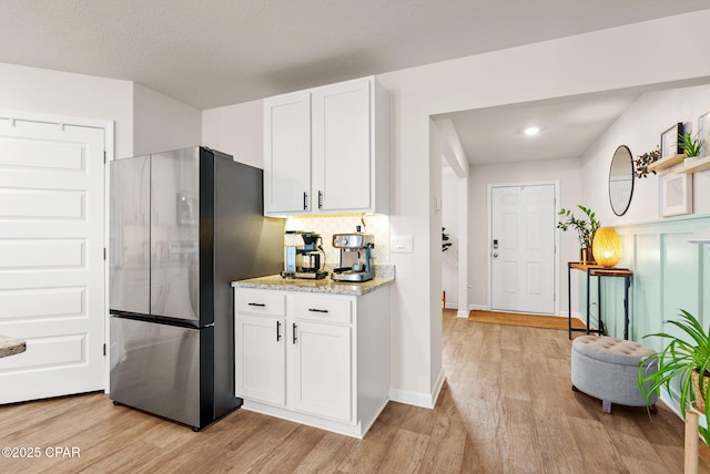 kitchen featuring white cabinets, backsplash, light wood-style floors, and freestanding refrigerator