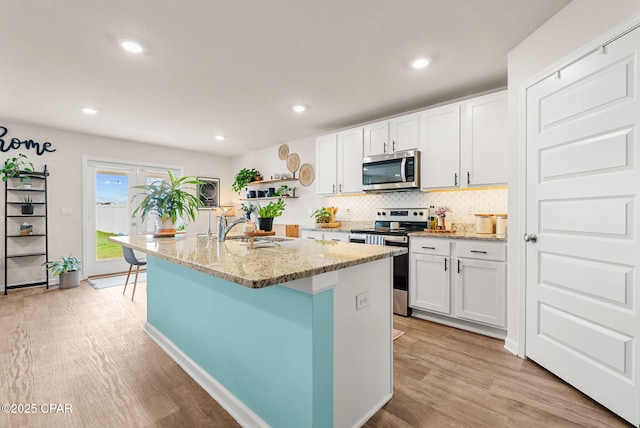 kitchen with a sink, tasteful backsplash, white cabinetry, stainless steel appliances, and light wood-style floors