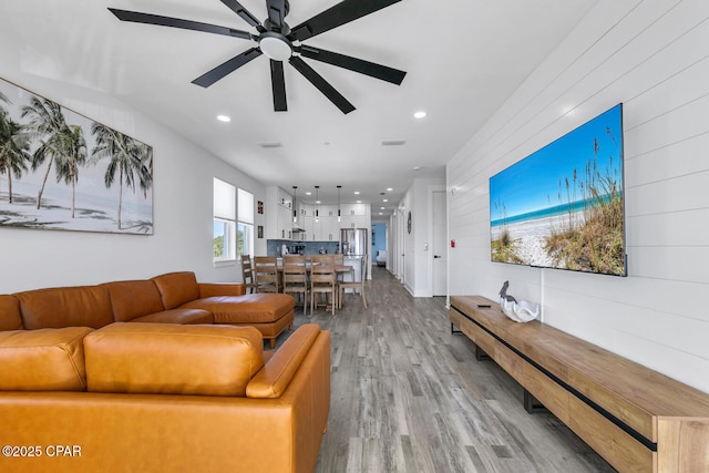 living area with wooden walls, recessed lighting, light wood-type flooring, and ceiling fan