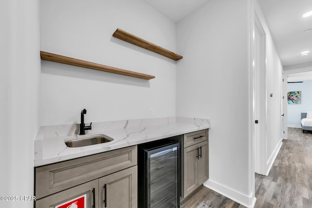 bar with light wood-type flooring, beverage cooler, a sink, baseboards, and wet bar