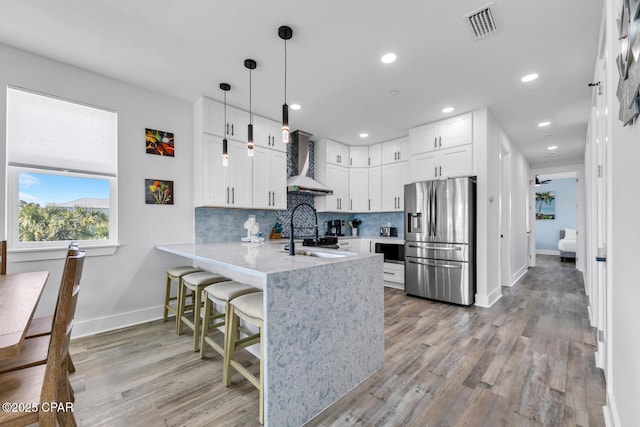kitchen with visible vents, a sink, stainless steel fridge, a peninsula, and wall chimney exhaust hood