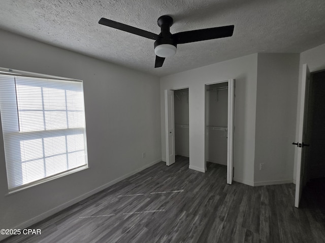 unfurnished bedroom featuring two closets, a ceiling fan, a textured ceiling, dark wood finished floors, and baseboards