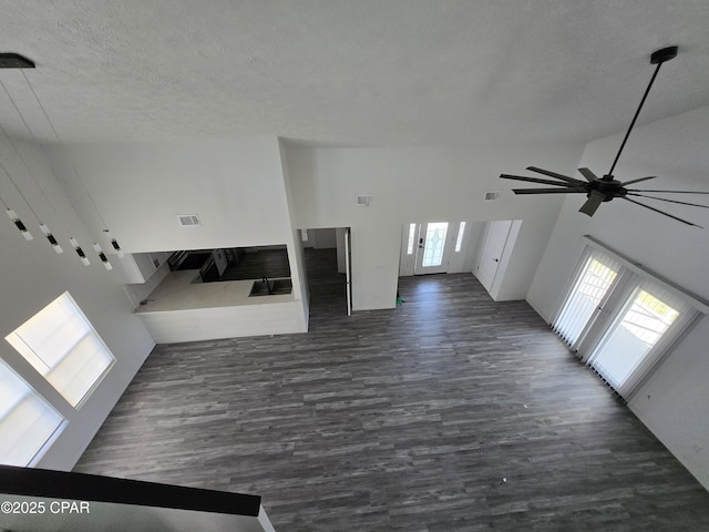 unfurnished living room featuring visible vents, a textured ceiling, dark wood-style floors, and a ceiling fan