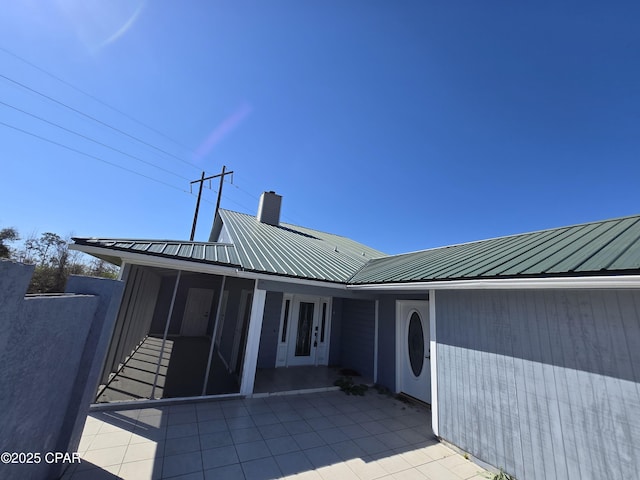 exterior space featuring a patio area, a chimney, metal roof, and a sunroom