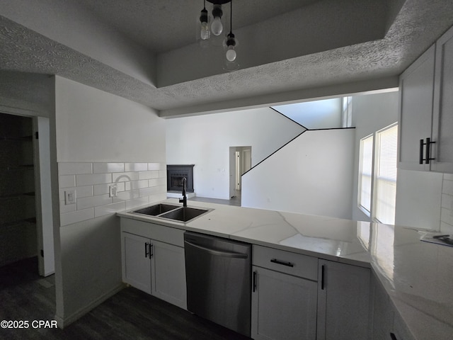 kitchen featuring a sink, stainless steel dishwasher, a peninsula, and a textured ceiling