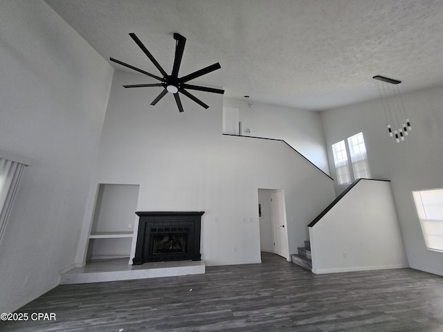 unfurnished living room with a fireplace with raised hearth, a textured ceiling, wood finished floors, a towering ceiling, and stairs