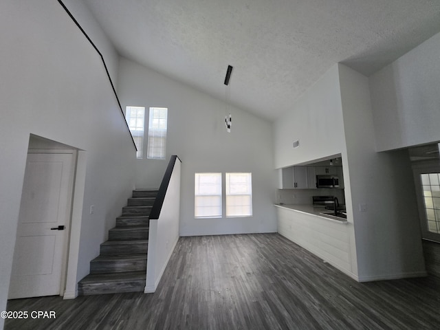 stairway with high vaulted ceiling, wood finished floors, and a textured ceiling