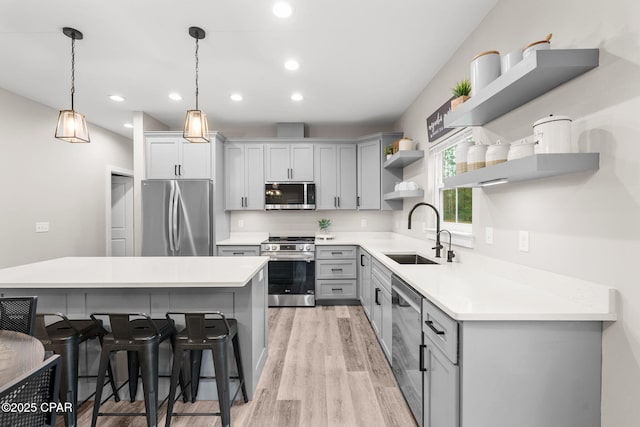 kitchen featuring a breakfast bar, gray cabinetry, a sink, open shelves, and appliances with stainless steel finishes