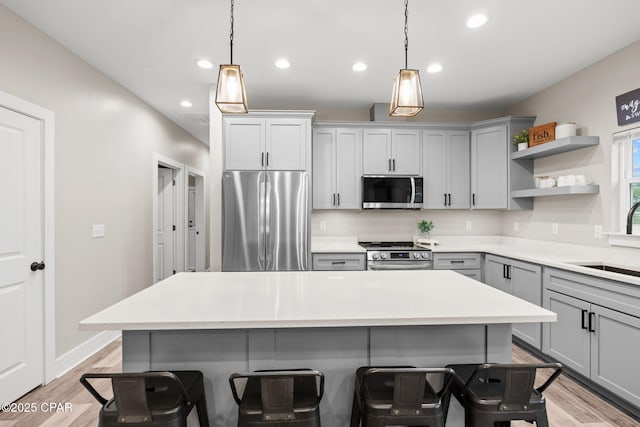 kitchen with a sink, a kitchen breakfast bar, gray cabinets, and stainless steel appliances