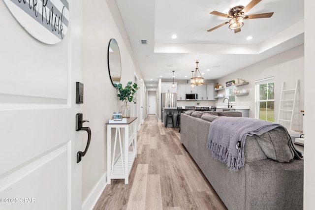 living area with visible vents, recessed lighting, light wood-style floors, and a tray ceiling