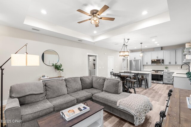 living room featuring a ceiling fan, visible vents, light wood finished floors, a tray ceiling, and recessed lighting