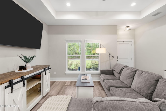 living room with visible vents, light wood-style flooring, a tray ceiling, recessed lighting, and baseboards