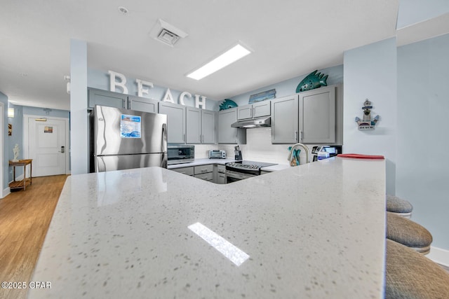 kitchen featuring gray cabinetry, light stone countertops, under cabinet range hood, and stainless steel appliances