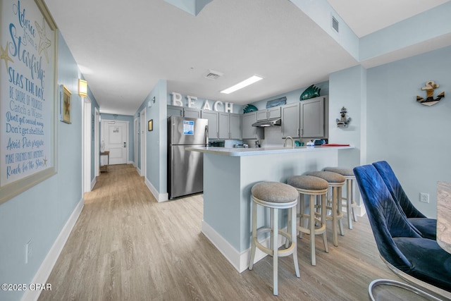 kitchen with a breakfast bar area, light wood-type flooring, gray cabinets, a peninsula, and freestanding refrigerator