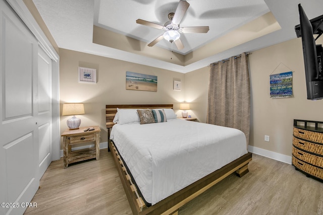 bedroom with a tray ceiling, baseboards, light wood-style floors, and ceiling fan