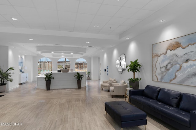 living room featuring light wood finished floors, a paneled ceiling, a raised ceiling, and baseboards