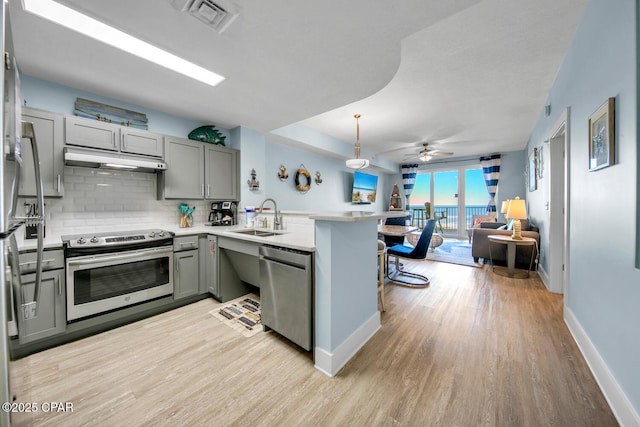 kitchen featuring under cabinet range hood, gray cabinets, a peninsula, stainless steel appliances, and a sink