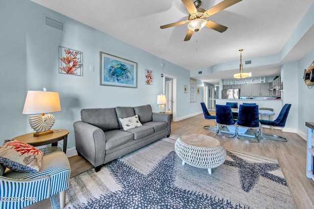 living area with baseboards, visible vents, light wood finished floors, and ceiling fan