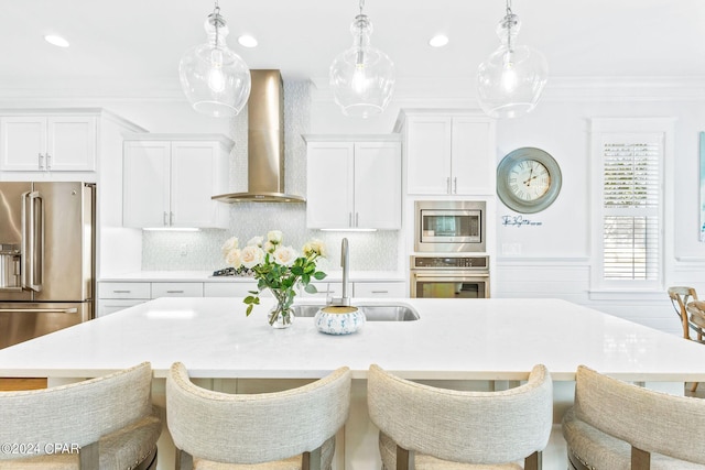 kitchen featuring a sink, light countertops, appliances with stainless steel finishes, crown molding, and wall chimney range hood