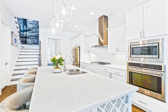 kitchen featuring a breakfast bar, a center island with sink, a sink, stainless steel appliances, and wall chimney range hood