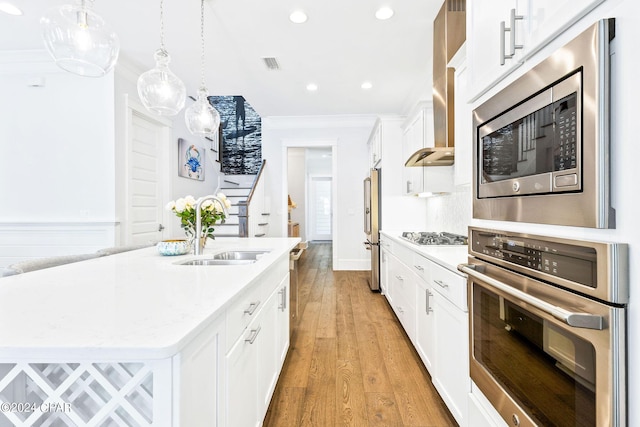 kitchen featuring a sink, appliances with stainless steel finishes, white cabinetry, crown molding, and wall chimney range hood