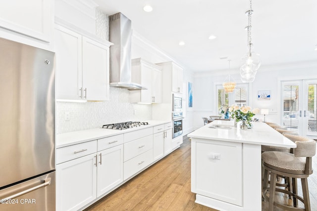 kitchen featuring a sink, white cabinets, appliances with stainless steel finishes, crown molding, and wall chimney range hood