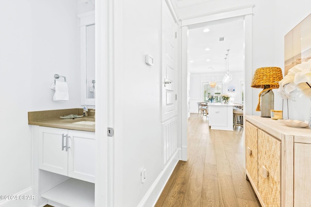 hallway featuring light wood finished floors, visible vents, and a sink