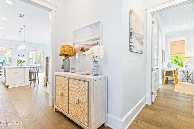 hall featuring light wood-type flooring, visible vents, baseboards, and crown molding