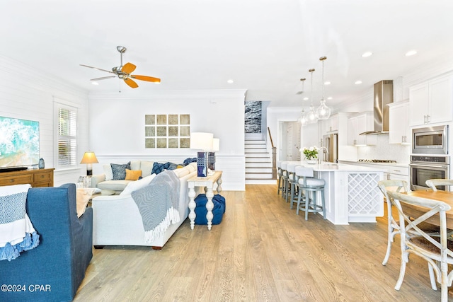 living area with stairway, ornamental molding, a ceiling fan, and light wood-style flooring