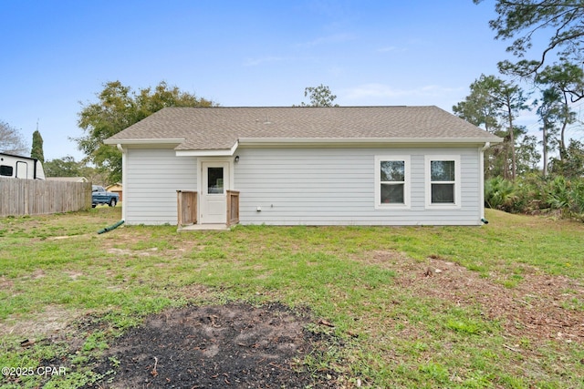 back of property featuring roof with shingles, a yard, and fence