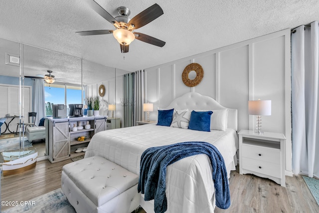 bedroom with ceiling fan, a decorative wall, wood finished floors, and a textured ceiling