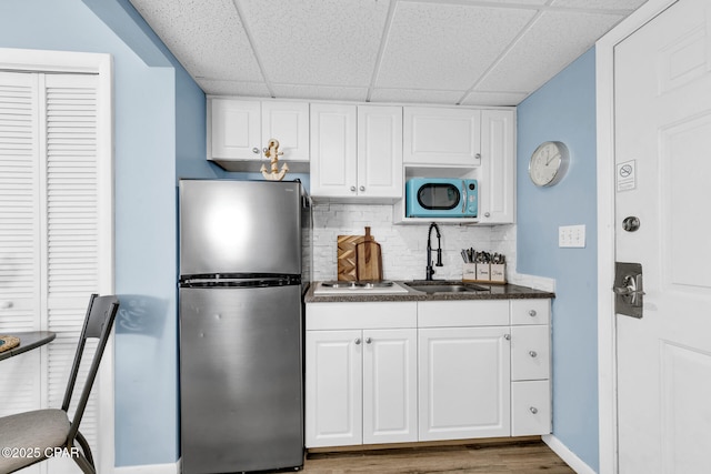 kitchen with freestanding refrigerator, a sink, white cabinets, dark countertops, and backsplash