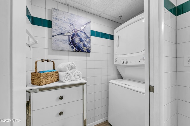 washroom featuring laundry area, stacked washer and clothes dryer, and tile walls