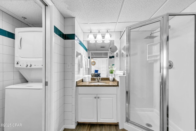 full bath featuring a shower stall, tile walls, stacked washer / drying machine, and a paneled ceiling