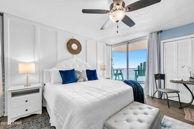 bedroom featuring access to outside, a textured ceiling, wood finished floors, floor to ceiling windows, and ceiling fan