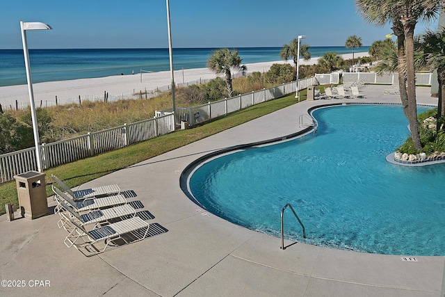 pool featuring a patio area, a water view, a view of the beach, and fence