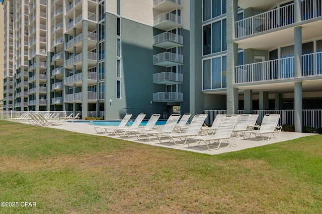 view of property's community featuring a pool, a lawn, a patio, and fence