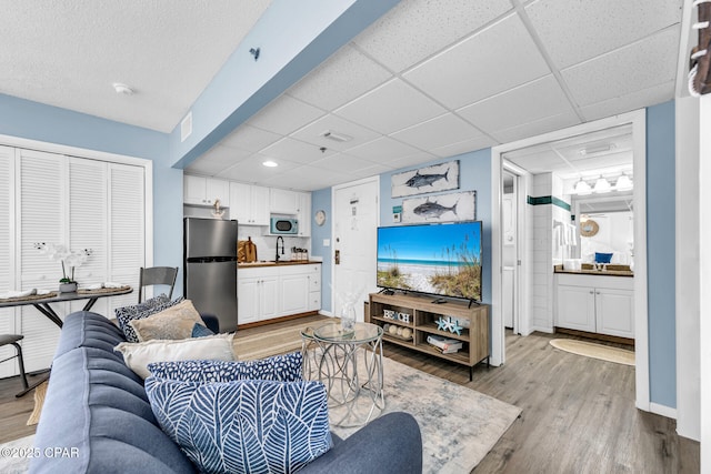 living room featuring a drop ceiling, baseboards, visible vents, and light wood-style flooring