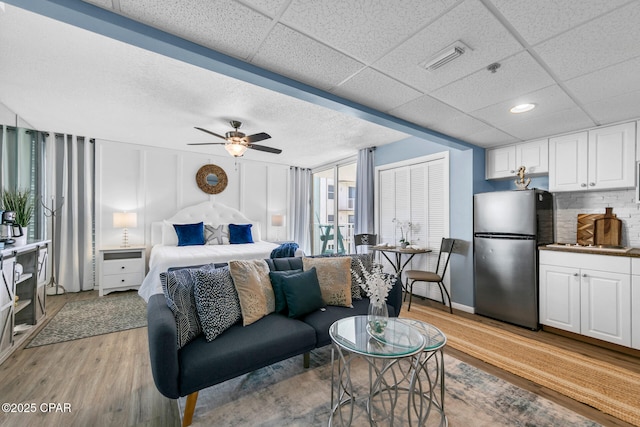 bedroom featuring visible vents, ceiling fan, a drop ceiling, freestanding refrigerator, and light wood-style floors