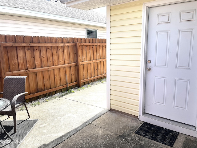 entrance to property with a shingled roof, a patio, and fence