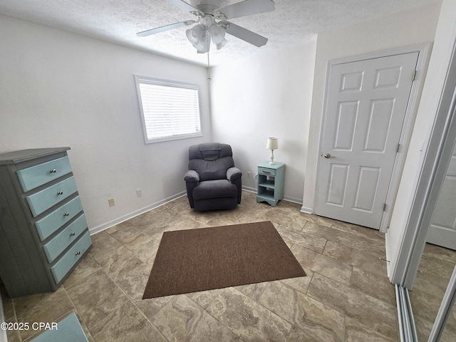 living area with ceiling fan, a textured ceiling, and baseboards