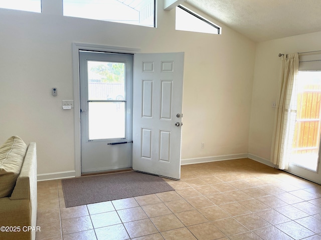 entrance foyer featuring vaulted ceiling, light tile patterned flooring, baseboards, and plenty of natural light