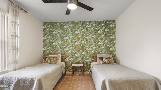 bedroom featuring a ceiling fan, an accent wall, and wallpapered walls