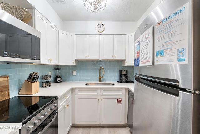 kitchen with decorative backsplash, appliances with stainless steel finishes, light countertops, white cabinets, and a sink